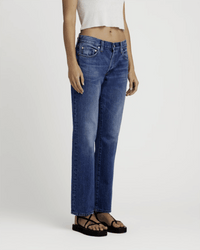 A person wears the Edwin Simone in Idle high-waisted indigo straight leg jeans, paired with a white sleeveless crop top and black sandals, standing against a plain light background with their head out of frame.