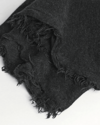 A close-up of the Grisal Love Cashmere Scarf in Charcoal showcases its soft texture and frayed edges, exuding cozy luxury on a white surface.
