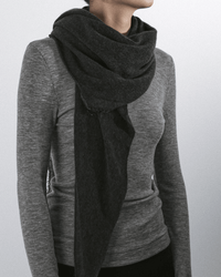 A person wears a fitted, ribbed grey long-sleeve shirt and the Grisal Love Cashmere Scarf in Charcoal, wrapped around their neck, standing against a plain light background.