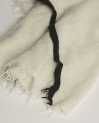 A close-up of the Rosa Cashmere Scarf in Milk X Black by Grisal shows its soft off-white fabric, frayed edges, and a single wavy black stripe, highlighting the artisanal texture distinctive to Grisal scarves.