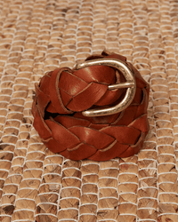 The Arthur Leather Belt in Brown by Hartford, featuring a braided genuine leather design and gold buckle, is displayed rolled up on a woven natural-colored mat.
