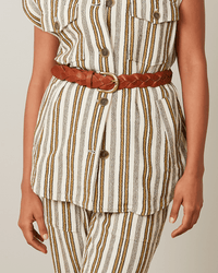 A person shown from shoulders to mid-thigh wears a white and yellow vertically striped outfit styled with the Hartford Arthur Leather Belt in Brown and brown buttons.