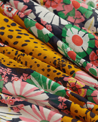 A close-up of the Inoui Editions Scarf 100 Pampa in Multicolor, a 100% cotton piece folded in layers, highlights vibrant pink, green, and white floral prints alongside yellow sections with black leopard spots.