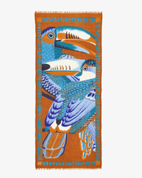 The Scarf 70 Toucan in Caramel by Inoui Editions is a rectangular orange wool scarf featuring blue and white birds with orange accents, a blue feather-like border, and fringed edges for a vibrant touch.