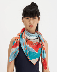 A woman with long black hair and blunt bangs wears the Inoui Editions Square 100 Yoga in Turquoise bandana draped around her neck, styled over a navy sleeveless top, set against a plain white background.