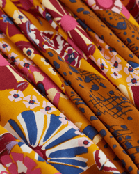 Close-up of pleated fabric from the Inoui Editions Square 130 Pampa in Fuchsia, showing a soft, textured silk-modal scarf with colorful floral and abstract patterns in mustard yellow, pink, blue, white, and red.
