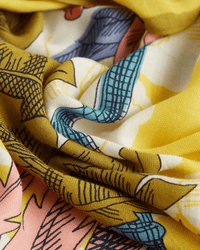 Close-up of colorful, patterned fabric from the Inoui Editions Square 130 Robinson in Yellow. The soft silk-cashmere scarf features yellow, blue, white, and pink sections with abstract geometric designs and black line accents.