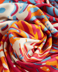 A close-up of the Square 130 Tango in Red by Inoui Editions shows its colorful silk modal blend with swirling red, orange, blue, and white patterns. The oversized bandana is softly folded, highlighting its vibrant abstract design and fluid texture.