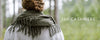 Person with brown hair wearing a gray coat and green fringe scarf stands in a forest. Text reads 