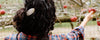 Person with curly hair, wearing a plaid shirt, reaching for a red apple on a tree branch.