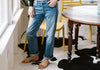 A person in jeans and sandals stands next to a wooden table, on a cowhide rug, near a window with natural light.