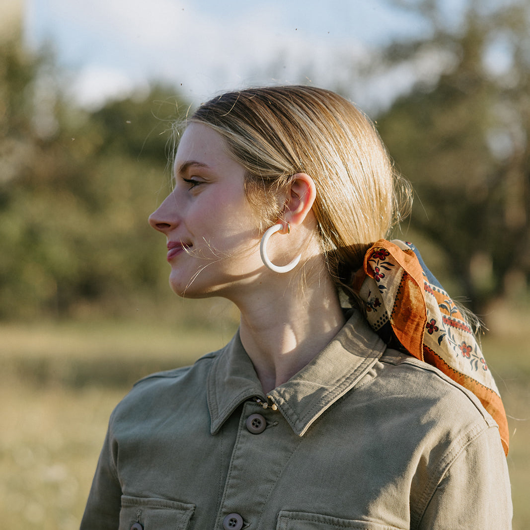 A woman with curly hair, wearing a white sweater and black scarf, smiles while looking to her left against a wooden interior background.