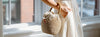 A person in blue jeans holds two reusable mesh bags, one containing oranges, standing against a white background.