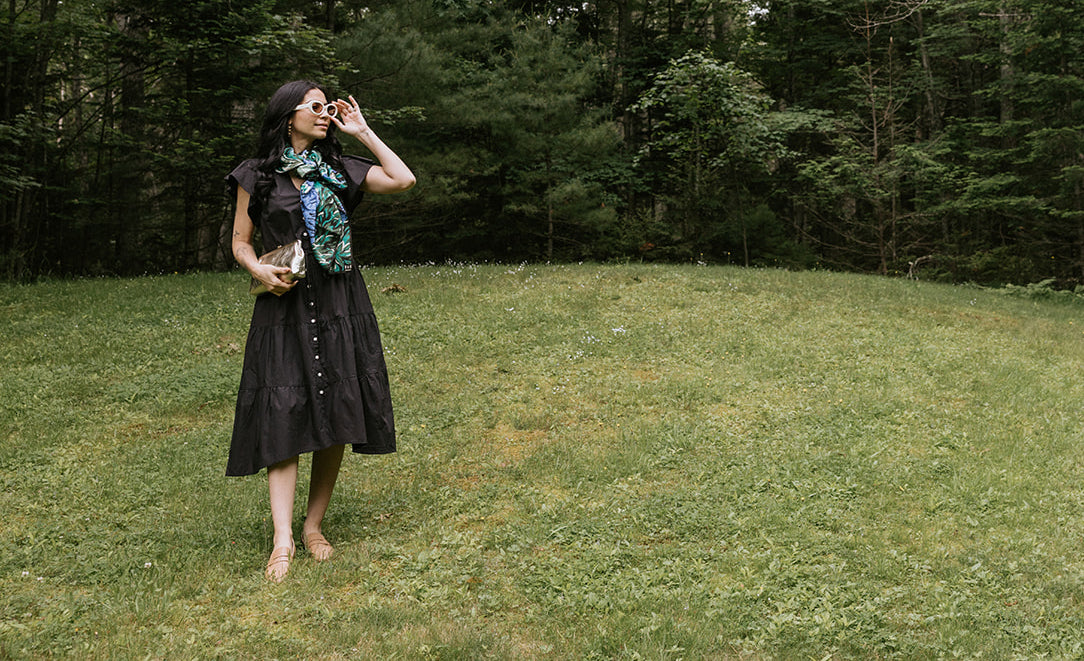 A person wearing a plaid shirt stands by a wooden fence adorned with blooming hydrangeas in a lush, green outdoor setting. A dark jacket is draped over the fence.