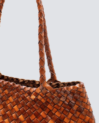 Close-up of a braided Santa Croce Bag Big in Tan leather weaving straps handle against a neutral background by Dragon Diffusion.