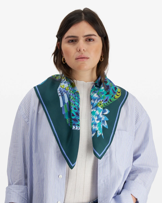 Woman in a striped shirt wearing an Inoui Editions Square / Carre 65 Hulule scarf in Emerald with a colorful pattern.