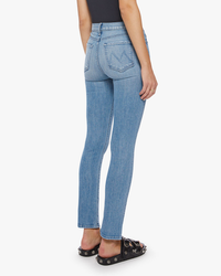 Woman wearing Mother Denim The Rascal Skimp in Punk Charming blue jeans with an ankle grazing inseam and black shoes with round embellishments from a rear side view.