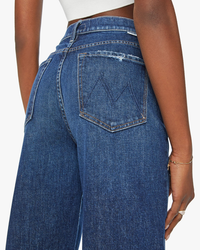 Close-up of a person wearing high-waisted blue denim jeans, focusing on the back pocket design of The Curbside Flood jeans in Yee Haw by Mother.