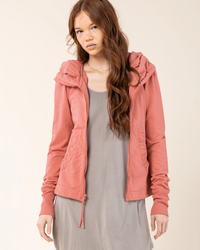 Young woman in a casual pink Prairie Underground Cloak Hoodie in Pink Guava and gray dress posing for the camera.