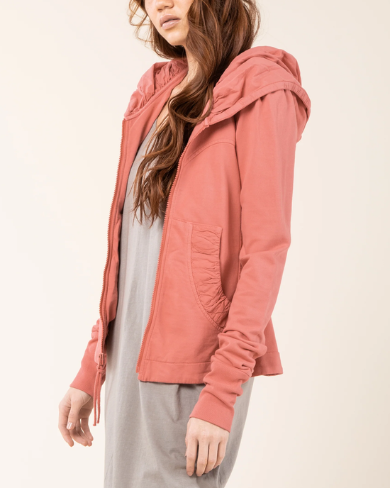 Woman wearing a pink Prairie Underground Cloak Hoodie in Pink Guava with a gray dress underneath, crafted from organic cotton.