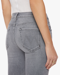 Close-up view of a woman wearing light-wash, high-waisted denim jeans with a distinct 'm' stitching on the back pocket, The Insider Crop Step Fray in Barely There by Mother.