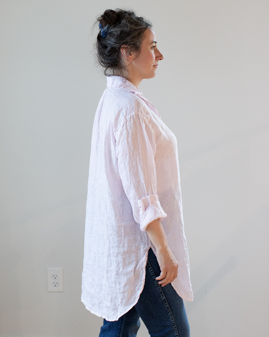 Profile view of a woman standing with her hand on her hip, wearing a white CP Shades Marella Tunic Blouse in Pink Stripe Linen.
