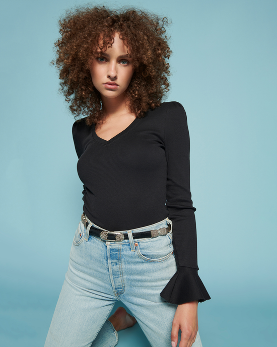 Woman with curly hair wearing a Nation LTD Sylvia Prim + Proper Tee in Jet Black and light blue jeans against a blue background.