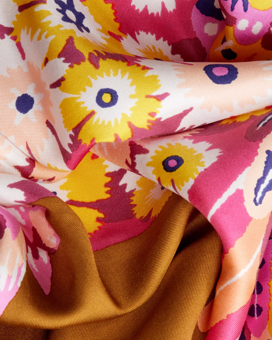 Close-up of a luxurious Inoui Editions Square / Carre 65 Hulule in Fuchsia scarf with pink, yellow, and purple patterns on a brown background.