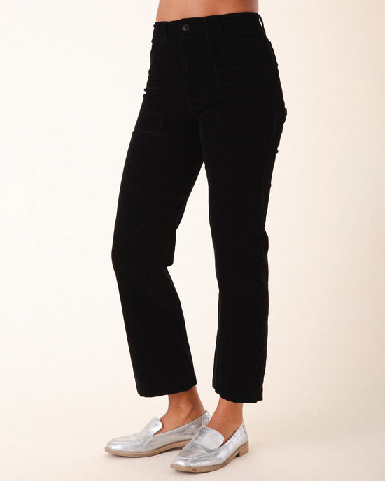 A person stands against a plain light background, showing only their lower torso and legs, wearing Prairie Underground's Corduroy Carpenter Pant in Black with silver loafers.