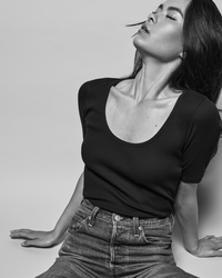 A black and white photo of a woman with eyes closed, tilting her head back, wearing a Nation LTD Lark Deep Scoop Tee in Jet Black and denim pants.
