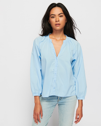 Woman wearing a Nation LTD Desire Dolman Button Up in Shirting and blue jeans standing against a white background.