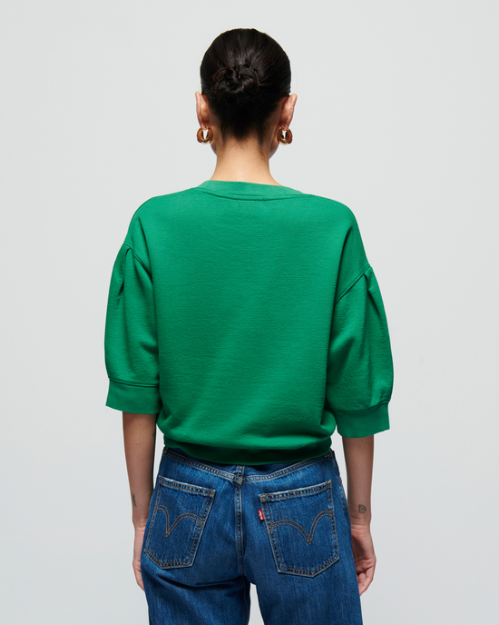 A woman in a Nation LTD Tate Crewneck Sweatshirt in Verdant Green and blue jeans, viewed from behind, standing against a plain background.