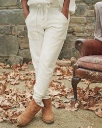 Woman standing in Eamon Jogger Sweatpants in Vintage White by Frank & Eileen and tan boots, with autumn leaves on the ground.