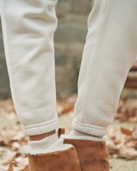 Person wearing Frank & Eileen's Eamon Jogger Sweatpants in Vintage White tucked into brown suede boots against an outdoor backdrop with autumn leaves.