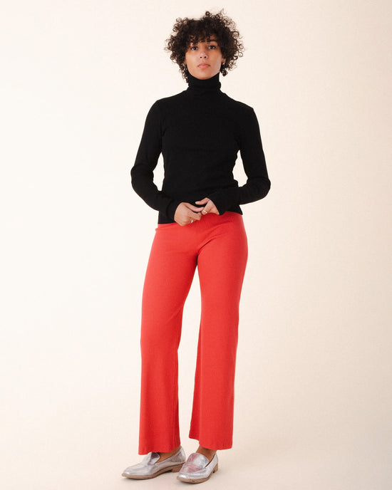 A person with curly hair wears the Prairie Underground Core Layer in Black with bright red pants and silver shoes, standing against a plain light background—an ideal layering piece for the modern wardrobe.
