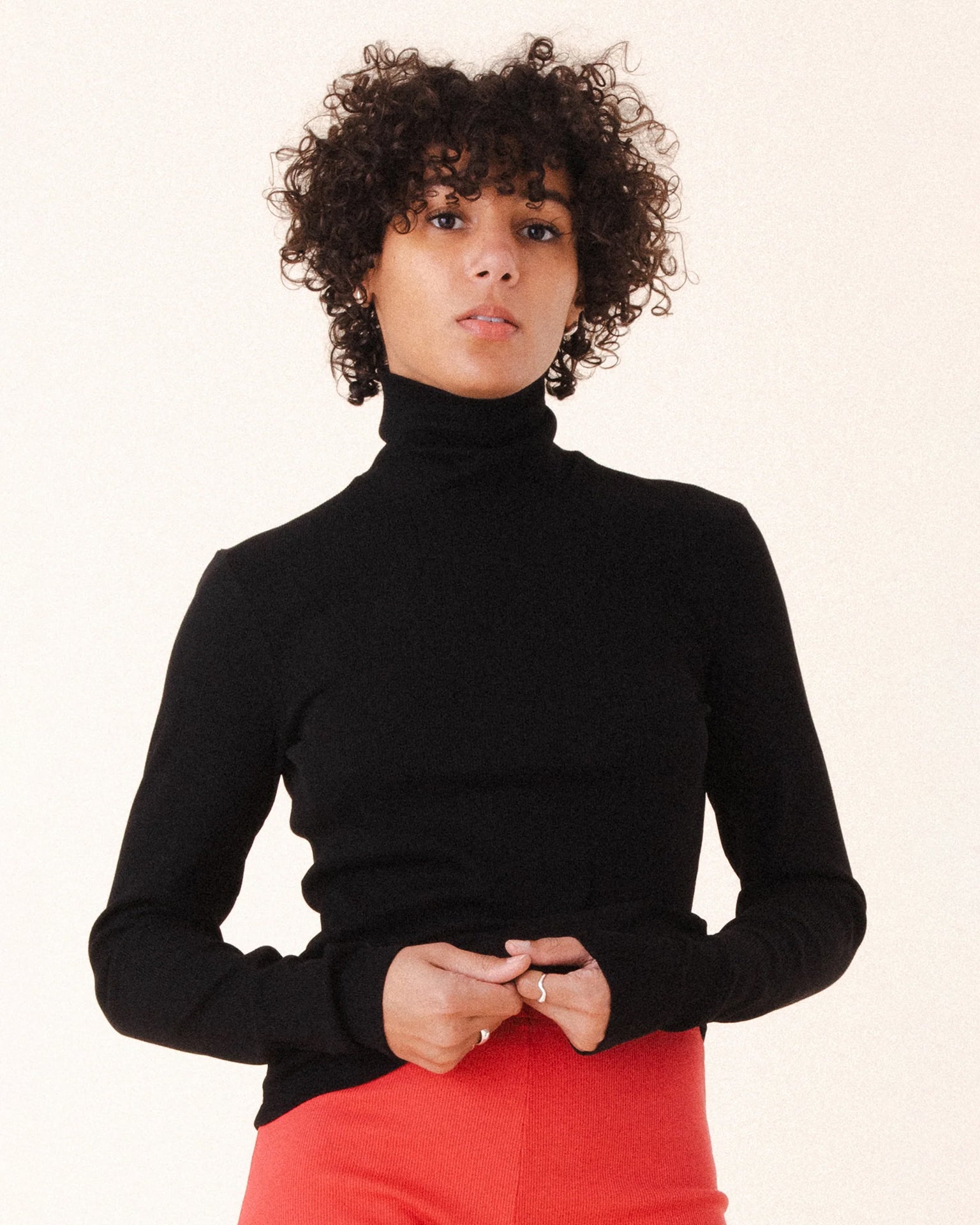 A person with short curly hair wears the Prairie Underground Core Layer in Black with red pants, standing against a plain light background and looking directly at the camera with a neutral expression.