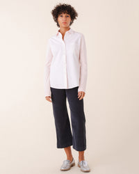 A person with short curly hair wears a light pink button-up shirt, Prairie Underground’s Knack Cords in Graphite, and silver loafers, standing against a plain light background.