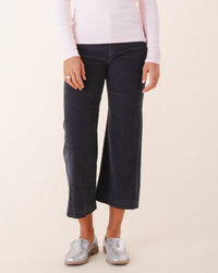 A person models Prairie Underground’s Knack Cords in Graphite—flared corduroy pants—paired with silver loafers and a light pink long-sleeve shirt, standing against a light background with relaxed hands at their sides. Only the lower body is shown.