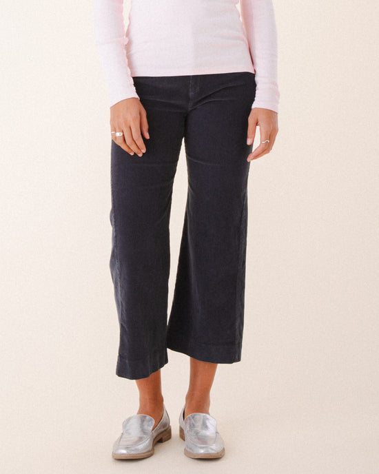 A person models Prairie Underground’s Knack Cords in Graphite—flared corduroy pants—paired with silver loafers and a light pink long-sleeve shirt, standing against a light background with relaxed hands at their sides. Only the lower body is shown.