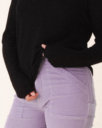 A person holds the hem of their black long-sleeve top, wearing Prairie Underground's Corduroy Carpenter Pant in Silver Mist. The image is cropped to show only the torso and upper legs.