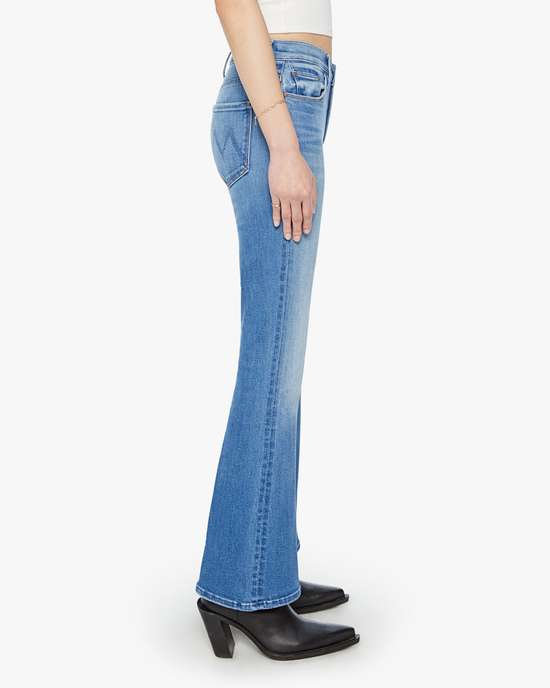 Side view of a person wearing Mother's blue stretch denim The Weekender in Layover, mid-rise flare leg jeans, and black heeled boots.