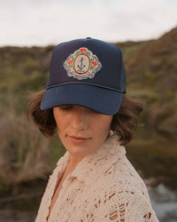 Woman wearing a decorated Freya Sally Sells Trucker hat in Navy outdoors, with a focus on the hat and blurred natural background.