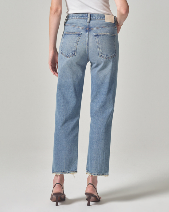 A person stands facing away from the camera modeling light blue, Citizens of Humanity Florence Wide Straight in Fontana jeans with frayed hems and brown strappy heels.