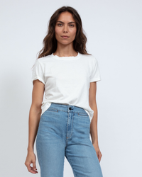 Woman in white 100% cotton ASKK NY Classic Tee in Ivory and blue jeans standing against a plain background, looking directly at the camera.