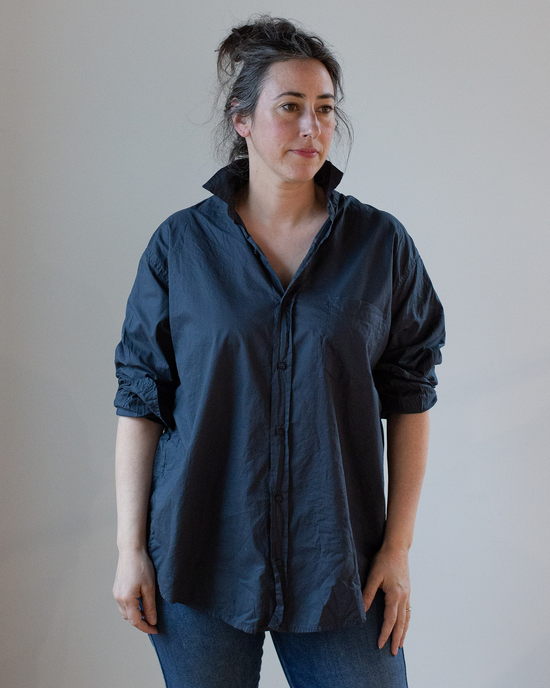 Woman standing casually in an oversized button-up CP Shades Joss 1 Pocket in Ink Cotton Oxford shirt and jeans with her hair tied back.