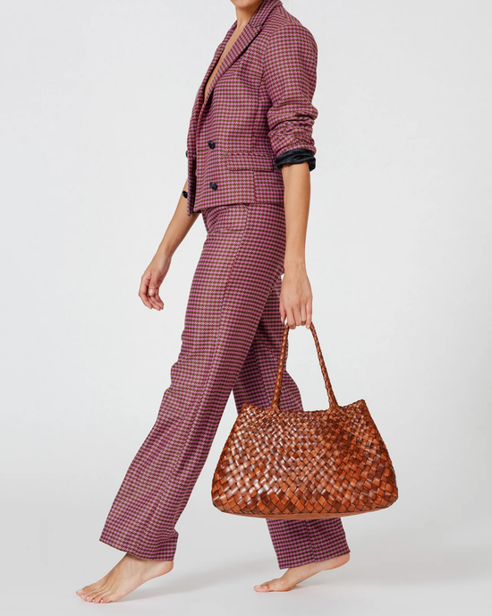 Woman showcasing a houndstooth patterned suit and holding a Dragon Diffusion Santa Croce Bag Big in Tan with leather weaving straps.