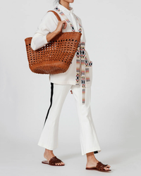 Woman in white attire holding a large Dragon Diffusion Cannage Market XL in Tan handwoven leather tote bag.