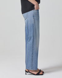 Person standing sideways wearing Citizens of Humanity Neve Low Slung Relaxed in Mist Blue denim jeans made from organic cotton and black heeled sandals.