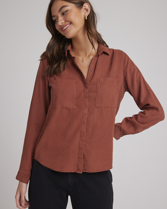 Woman smiling and posing in a rust-colored Bella Dahl Two Pocket Classic Button Down in Autumn Amber featuring front button closure and chest pockets, made from Tencel.