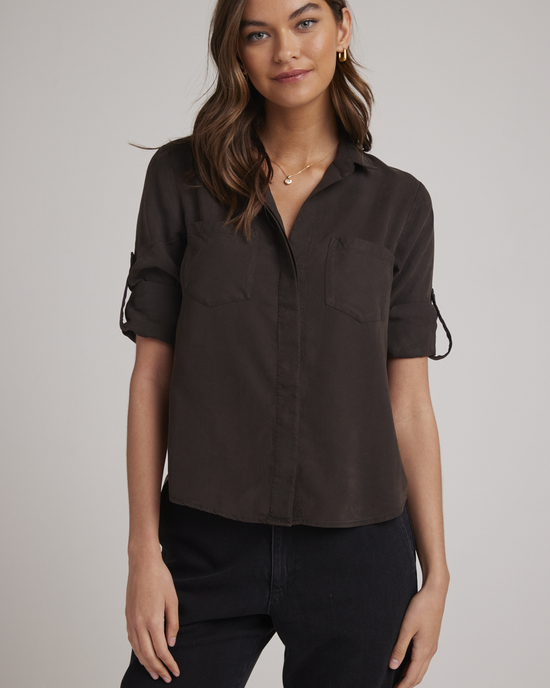 Woman wearing a casual Tencel Bella Dahl Split Back Button Down in Quartz Brown shirt with rolled-up sleeves, split back button down detail, and black pants.